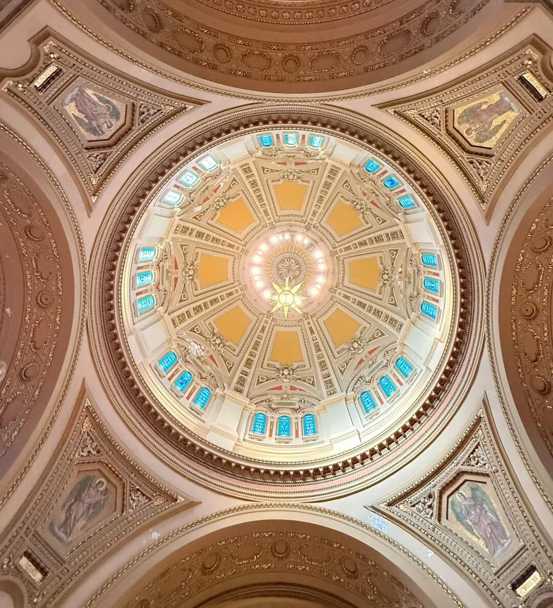 Warm cream and gold interior dome with stained glass and an eight-pointed chandelier