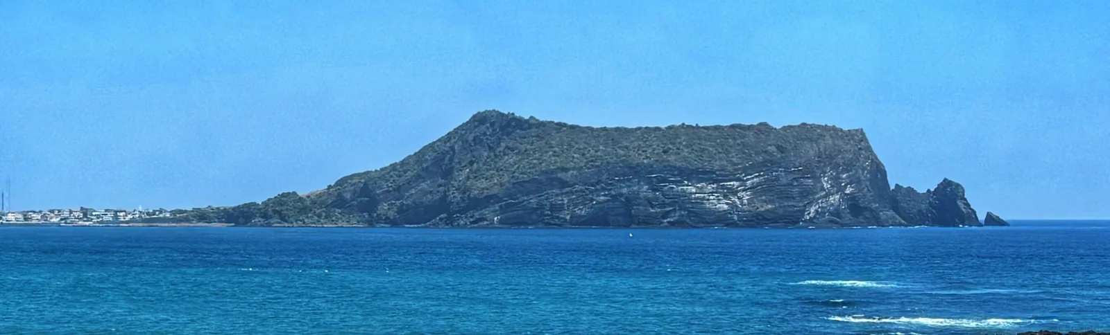 A volcanic hill rising across the blue water on Jeju Island