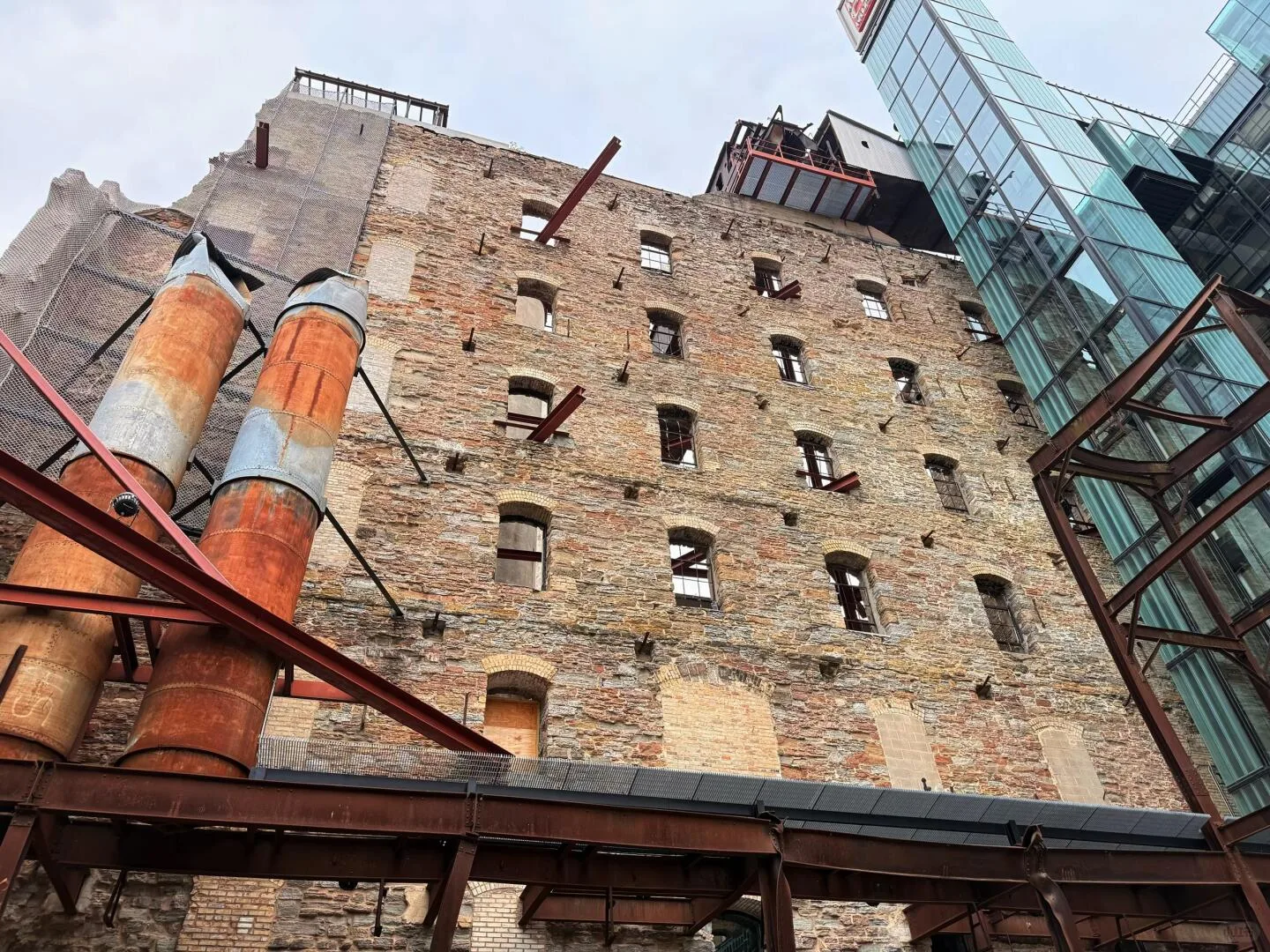 Stone wall, rusted pipes, and modern glass structures at the Mill City ruins