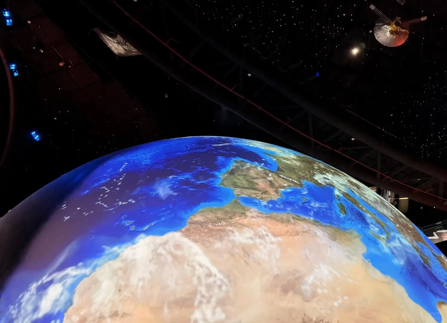 Large illuminated Earth visualization beneath hanging spacecraft